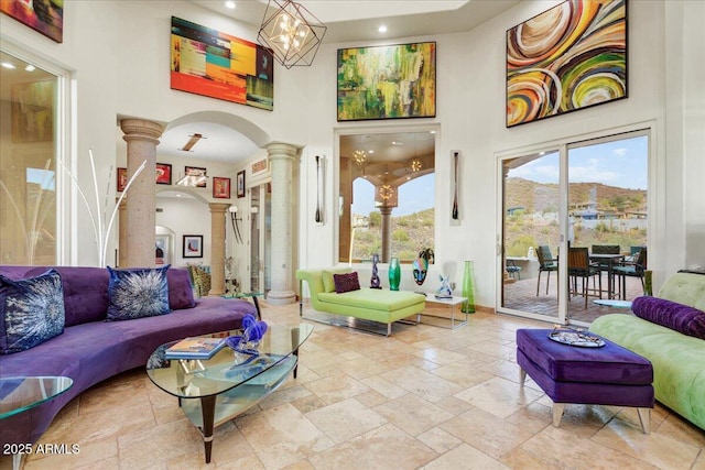 living room with arched walkways, a notable chandelier, decorative columns, stone tile floors, and a towering ceiling