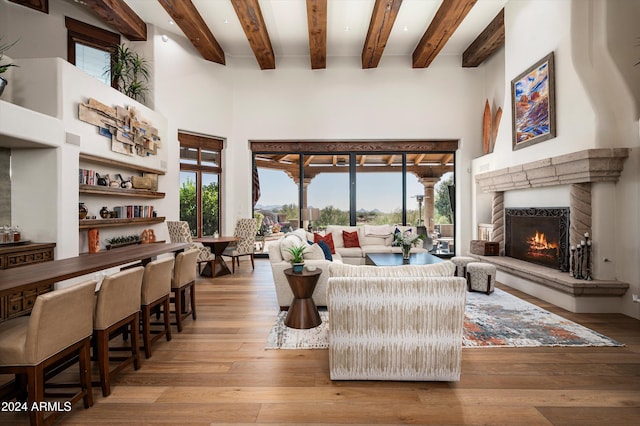 living room with plenty of natural light, beam ceiling, a towering ceiling, and light hardwood / wood-style flooring