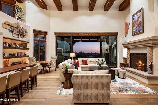 living room featuring beam ceiling, a towering ceiling, a high end fireplace, and light hardwood / wood-style flooring