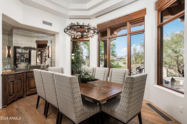 dining room featuring ornamental molding, light hardwood / wood-style flooring, a raised ceiling, and a healthy amount of sunlight