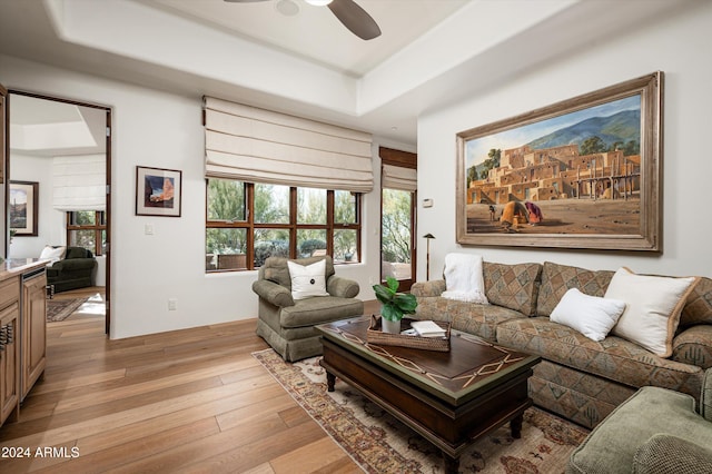 living room with a raised ceiling, ceiling fan, and light wood-type flooring