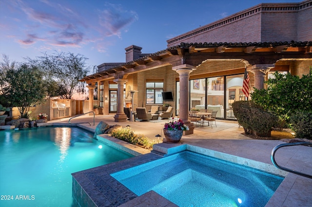 pool at dusk featuring an in ground hot tub, an outdoor living space, a patio area, and exterior kitchen