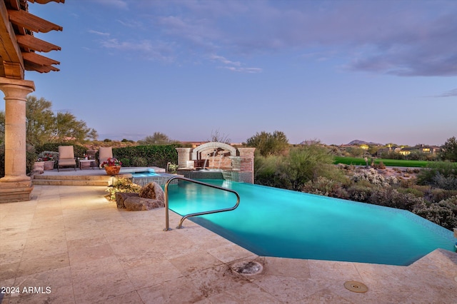 pool at dusk with an in ground hot tub, a patio, and pool water feature