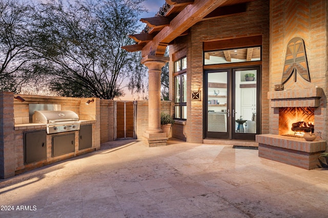 exterior entry at dusk featuring a patio, a large fireplace, and area for grilling