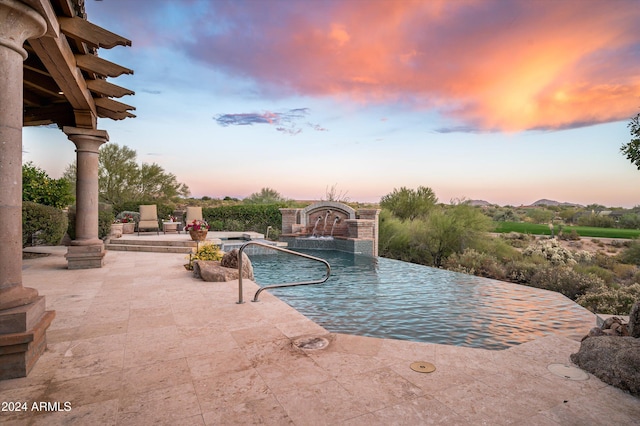 pool at dusk featuring pool water feature and a patio