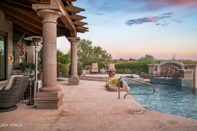 pool at dusk featuring pool water feature and a patio