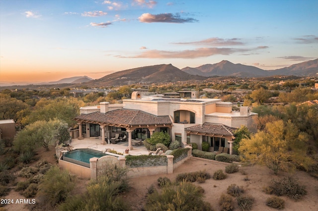 back house at dusk with a mountain view and a patio area