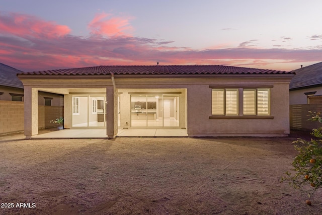 rear view of property featuring a tiled roof, stucco siding, a patio, and fence