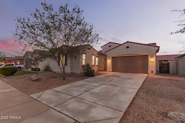 view of front facade with a tiled roof, stucco siding, driveway, an attached garage, and a gate