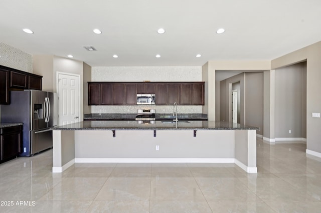 kitchen with visible vents, dark stone counters, a large island, stainless steel appliances, and a sink