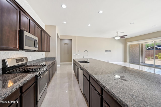 kitchen featuring dark brown cabinets, baseboards, dark stone counters, appliances with stainless steel finishes, and a sink