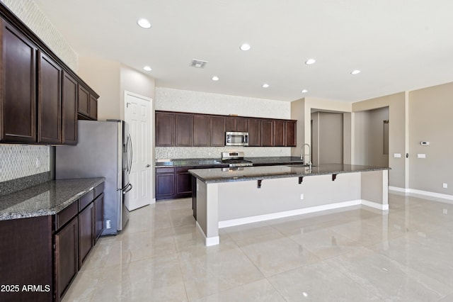 kitchen featuring a large island, a sink, dark stone countertops, stainless steel appliances, and a breakfast bar area