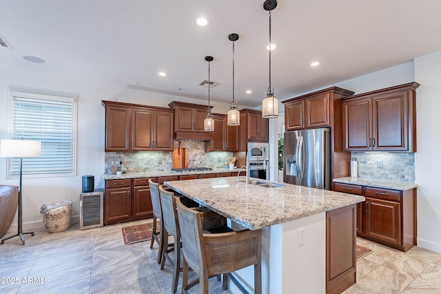 13719 W Amberwing St, Peoria, AZ 85383 - kitchen with appliances with stainless steel finishes, a sink, backsplash, a kitchen island with sink, and hanging light fixtures