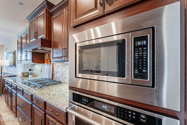 13719 W Amberwing St, Peoria, AZ 85383 - kitchen with appliances with stainless steel finishes, under cabinet range hood, backsplash, and light stone countertops
