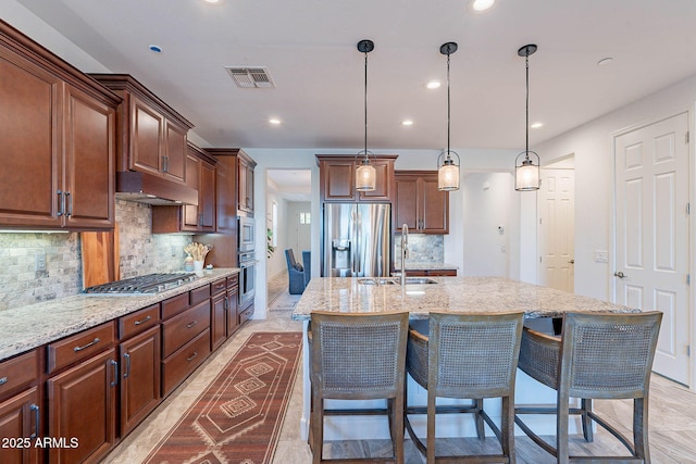 13719 W Amberwing St, Peoria, AZ 85383 - kitchen featuring appliances with stainless steel finishes, a sink, under cabinet range hood, tasteful backsplash, and a kitchen island with sink