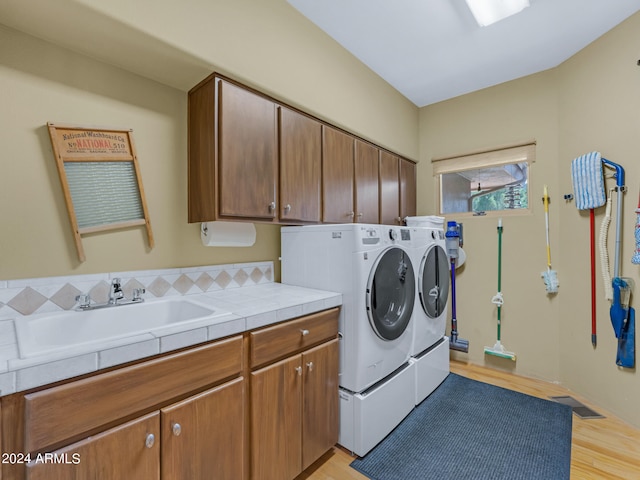 laundry area featuring washing machine and dryer, sink, light hardwood / wood-style floors, and cabinets