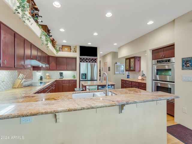 kitchen with kitchen peninsula, sink, stainless steel appliances, and light hardwood / wood-style flooring