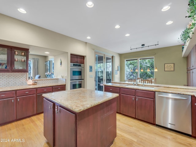 kitchen featuring sink, light hardwood / wood-style flooring, appliances with stainless steel finishes, a center island, and decorative backsplash