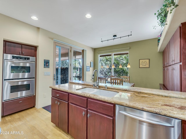 kitchen with light wood-type flooring, light stone countertops, stainless steel appliances, sink, and track lighting