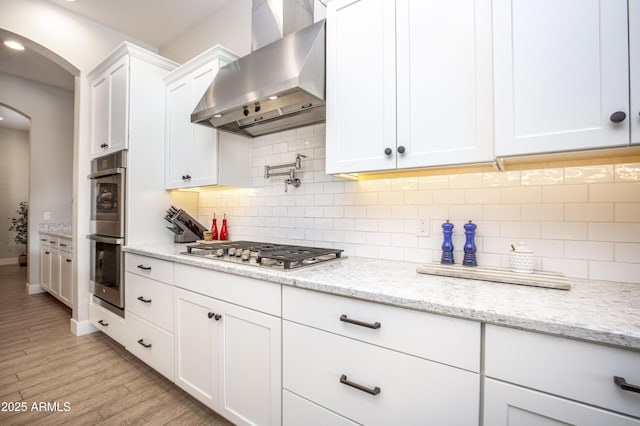 3118 E Gary Way, Phoenix, AZ 85042 - kitchen with wall chimney exhaust hood, arched walkways, appliances with stainless steel finishes, white cabinetry, and light wood finished floors