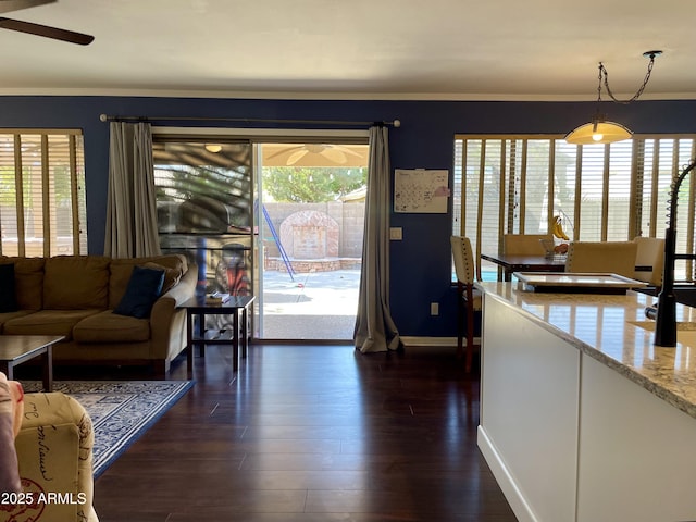 living room featuring dark wood-type flooring, a healthy amount of sunlight, baseboards, and a ceiling fan