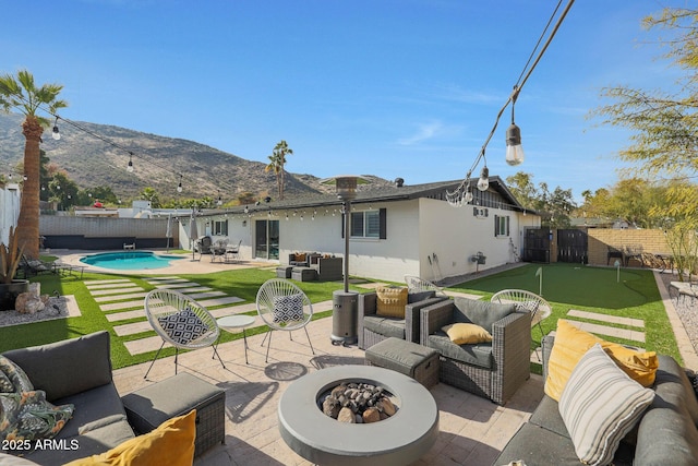 back of property with a mountain view, a fenced in pool, a patio, and an outdoor living space with a fire pit