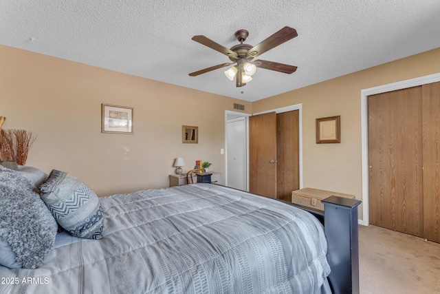 bedroom featuring a ceiling fan, visible vents, a textured ceiling, light colored carpet, and two closets