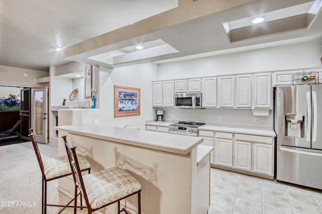 kitchen featuring light tile patterned floors, a breakfast bar area, white cabinetry, stainless steel appliances, and kitchen peninsula