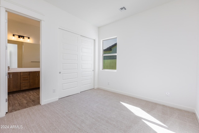 unfurnished bedroom with a closet, light carpet, and ensuite bath