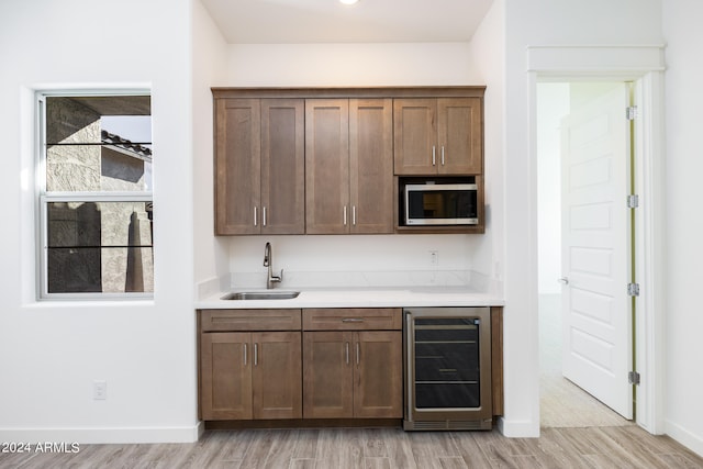 bar featuring light hardwood / wood-style floors, stainless steel microwave, sink, and wine cooler