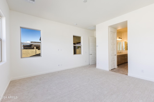 unfurnished bedroom with connected bathroom and light colored carpet