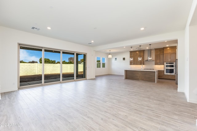 unfurnished living room featuring light hardwood / wood-style floors, sink, and a wealth of natural light