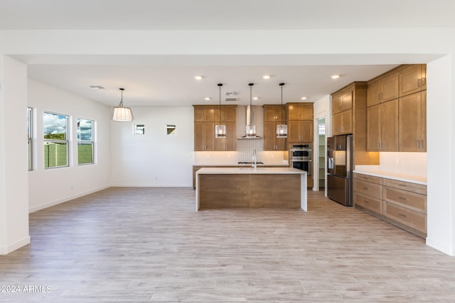 kitchen with pendant lighting, a center island with sink, wall chimney exhaust hood, light wood-type flooring, and stainless steel appliances