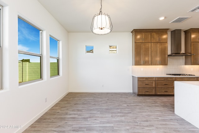 kitchen featuring tasteful backsplash, wall chimney exhaust hood, stainless steel gas cooktop, light hardwood / wood-style floors, and hanging light fixtures