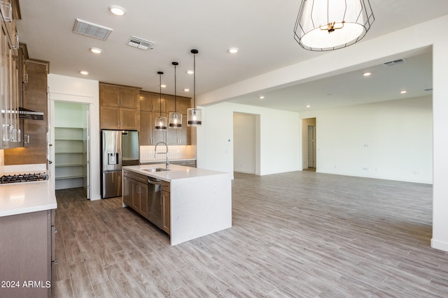 kitchen with stainless steel appliances, pendant lighting, decorative backsplash, a center island with sink, and light wood-type flooring