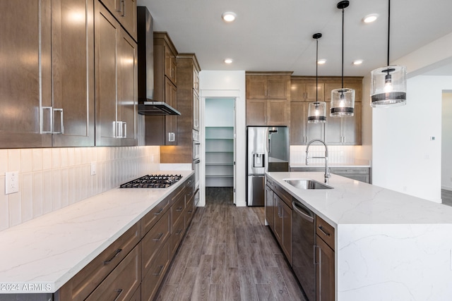 kitchen featuring wall chimney exhaust hood, stainless steel appliances, a kitchen island with sink, hardwood / wood-style flooring, and hanging light fixtures