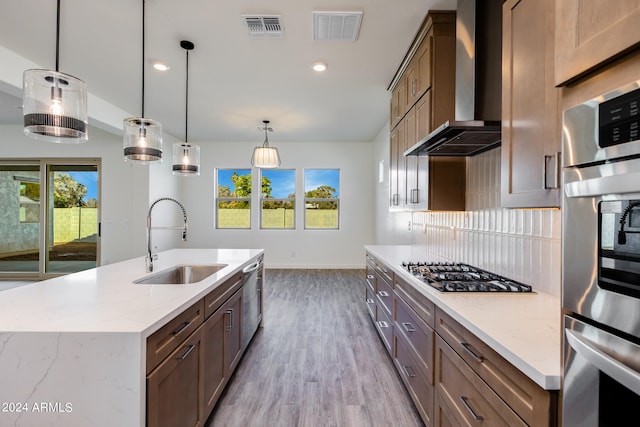 kitchen featuring appliances with stainless steel finishes, light wood-type flooring, sink, wall chimney range hood, and pendant lighting