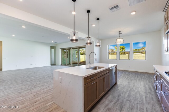 kitchen featuring sink, light hardwood / wood-style flooring, stainless steel dishwasher, an island with sink, and pendant lighting