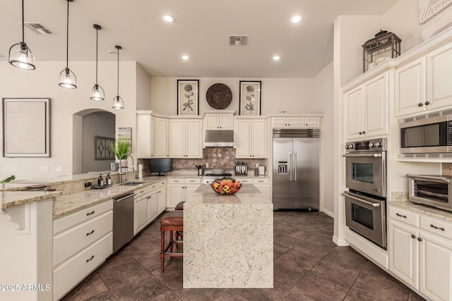 kitchen featuring light stone counters, built in appliances, decorative light fixtures, a kitchen breakfast bar, and kitchen peninsula