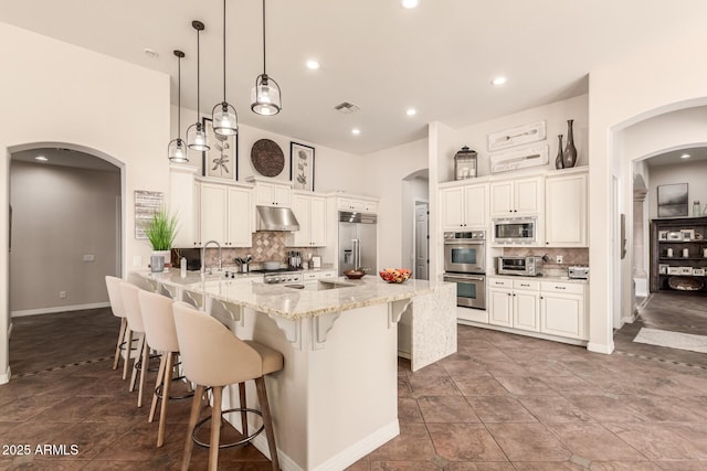 kitchen featuring a breakfast bar area, hanging light fixtures, built in appliances, light stone countertops, and decorative backsplash