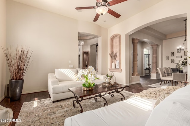 living room with ceiling fan with notable chandelier, dark wood-type flooring, and ornate columns