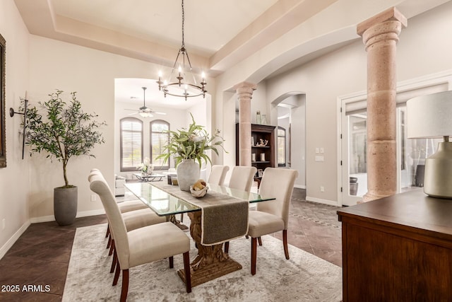 dining room featuring a tray ceiling, ceiling fan with notable chandelier, dark tile patterned floors, and ornate columns