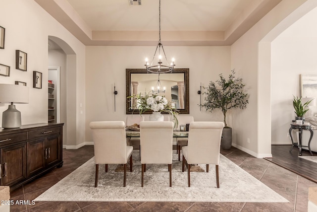 tiled dining area with a tray ceiling and a chandelier