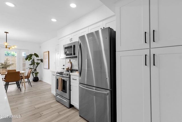 kitchen with light hardwood / wood-style flooring, white cabinets, a chandelier, and appliances with stainless steel finishes