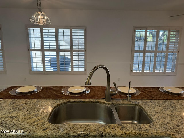 kitchen featuring plenty of natural light, stone countertops, sink, and hanging light fixtures