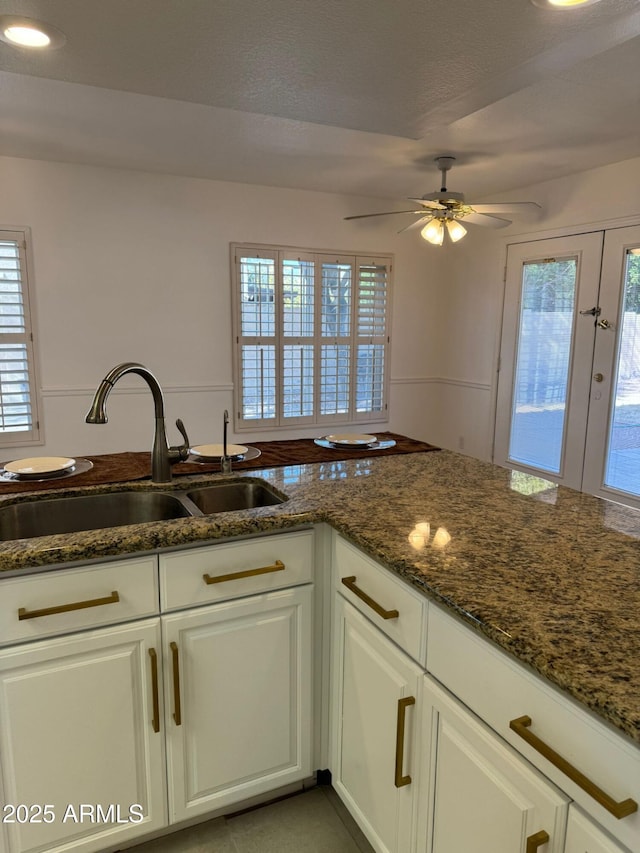 kitchen featuring white cabinetry, sink, dark stone counters, and ceiling fan