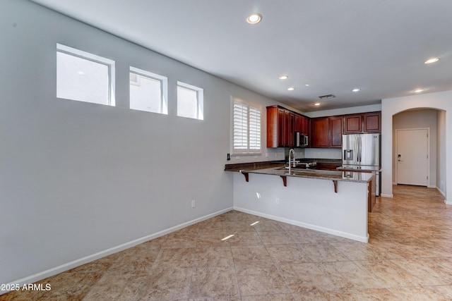 kitchen with dark stone countertops, a peninsula, arched walkways, a sink, and stainless steel appliances