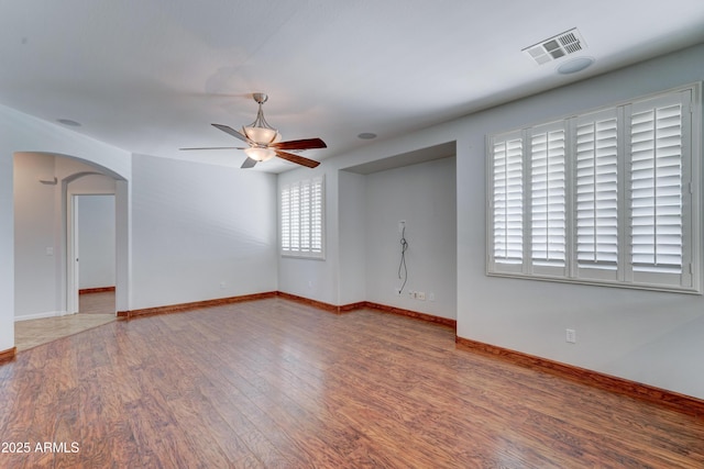 empty room featuring visible vents, baseboards, wood finished floors, arched walkways, and a ceiling fan