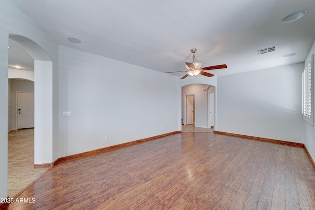 spare room with visible vents, baseboards, ceiling fan, light wood-style floors, and arched walkways