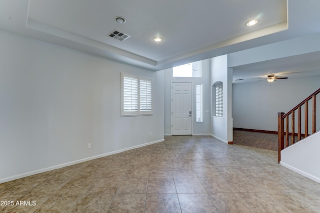 foyer featuring visible vents, a raised ceiling, baseboards, ceiling fan, and stairs